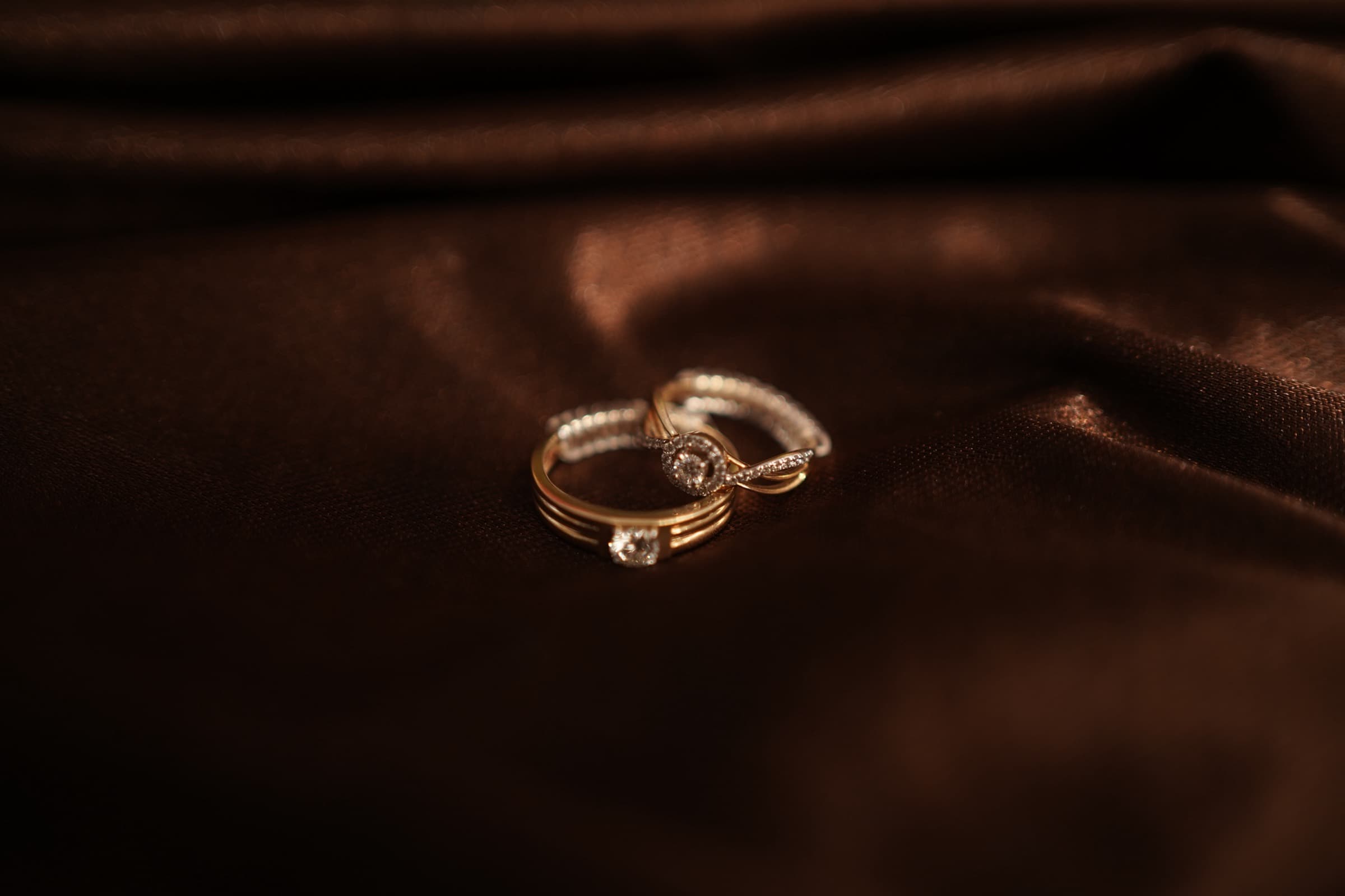 Mayank and Nancy's rings resting together on deep brown velvet